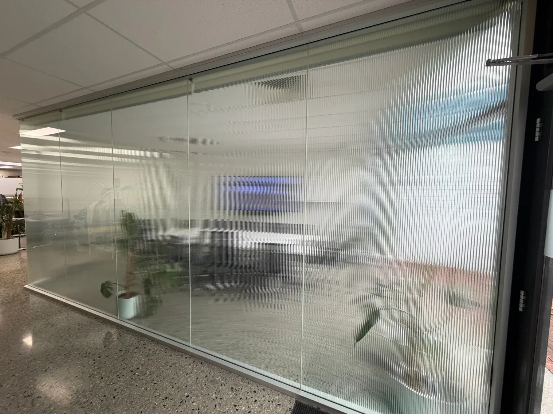 Meeting room viewed from outside its reeded glass partition, showing vertical ribs and softened furniture beyond